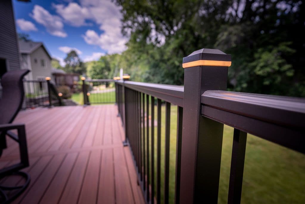 Close-up view of a dark metal deck railing featuring an illuminated post cap light on a composite deck surface.